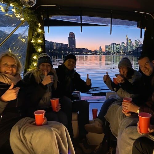 Kollegen bei einer Weihnachtsfeier mit der Firma in Frankfurt auf dem Main mit Glühwein auf einem Boot während die Sonne untergeht