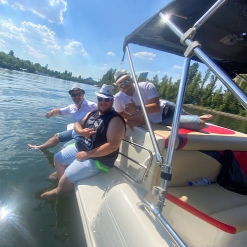 Männergruppe auf dem Partyboot Basic mit geschlsenem Verdeck, die zur Abkühlung die Beine im Wasser hängen lassen
