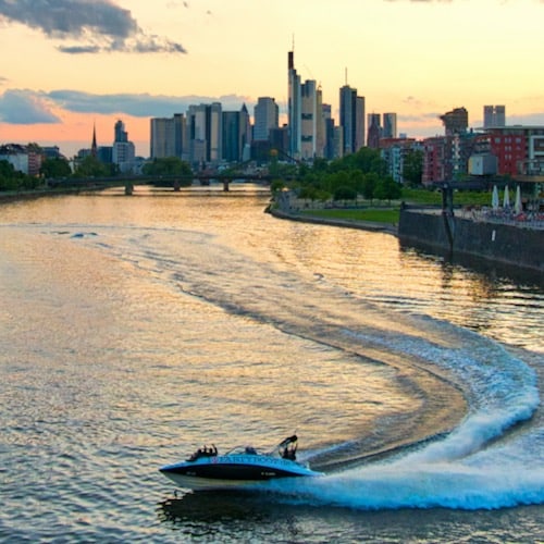 Speedboot in einer Kurve auf dem Main während die Sonne hinter der Skyline von Frankfurt untergeht